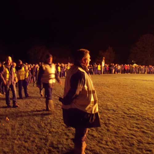 Marshall with walkie talkie  and crowd behind rope watching bonfire