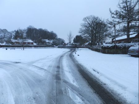 Snow scene  part of village green looking towards post office